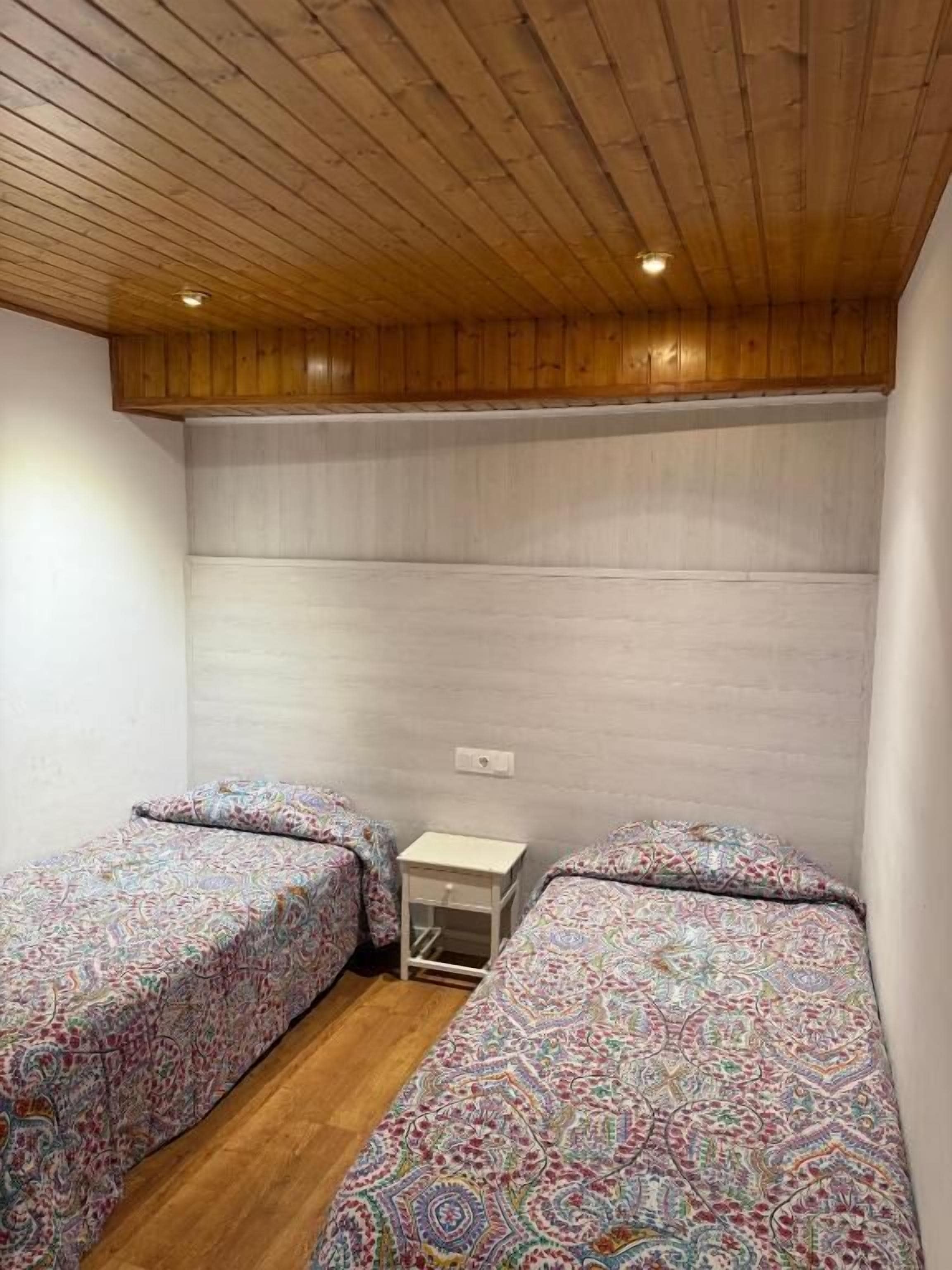 Quarto com duas camas, teto de madeira e uma pequena mesa de cabeceira.