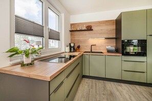 A modern kitchen with a wooden countertop, green cabinets, a built-in stove, and a window with blinds. - Modern Labiland vacation rental on the lagoon with a terrace and a magnificent view (Zirchow)