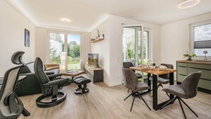 Uma sala de estar moderna com área de jantar, janelas amplas e vista para o verde.