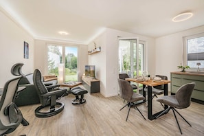 Ein modernes Wohnzimmer mit Essbereich, großen Fenstern und Blick auf Grünflächen.