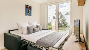 Quarto moderno com cama, almofadas, TV e janela com vista para o exterior.