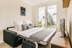 Ein modernes Schlafzimmer mit Bett, Kissen, Fernseher und einem Fenster mit Blick nach draußen.
