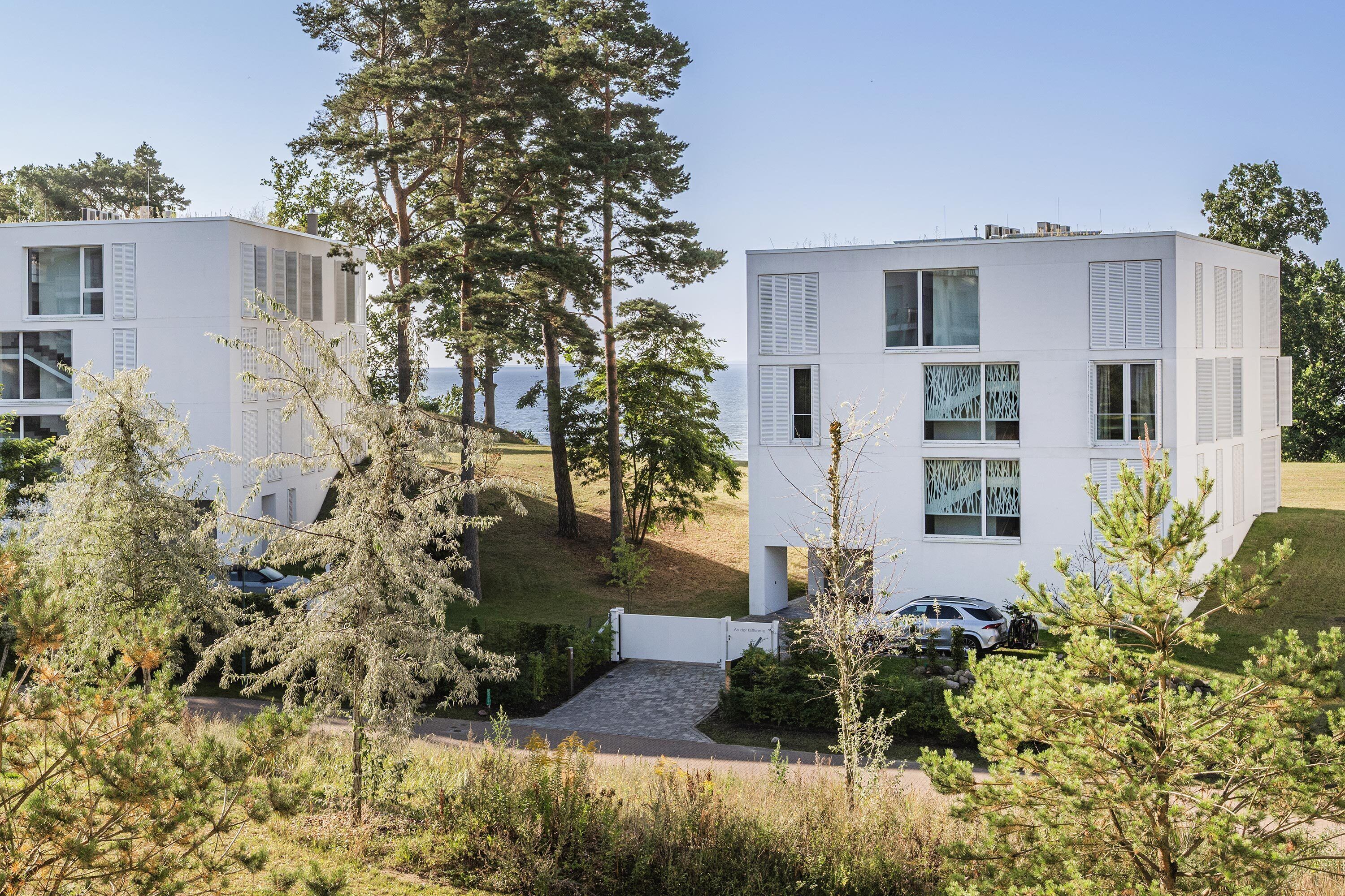 A modern two-story building with a flat roof, large windows, and a paved driveway.