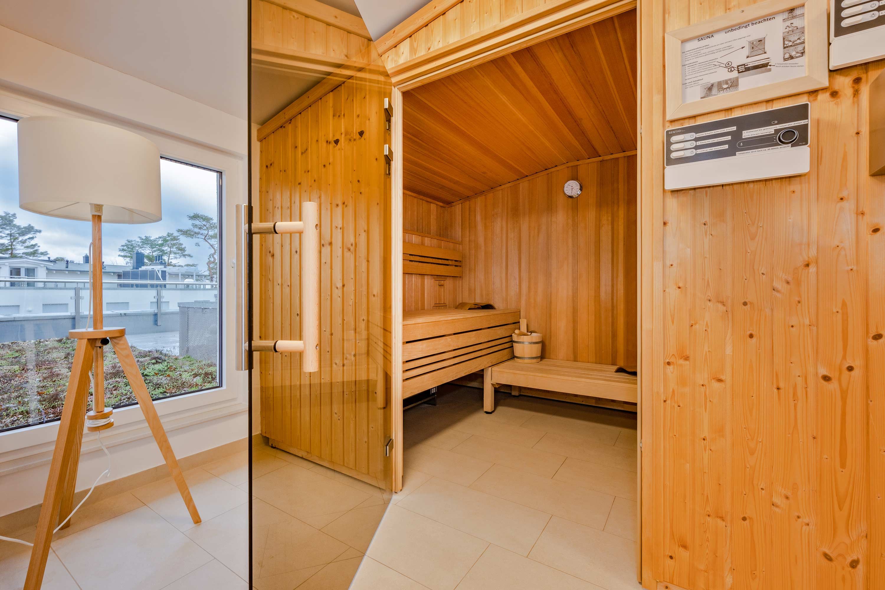 Un sauna aux murs et aux bancs en bois, doté d’un lampadaire sur trépied et d’une fenêtre offrant une vue agréable.