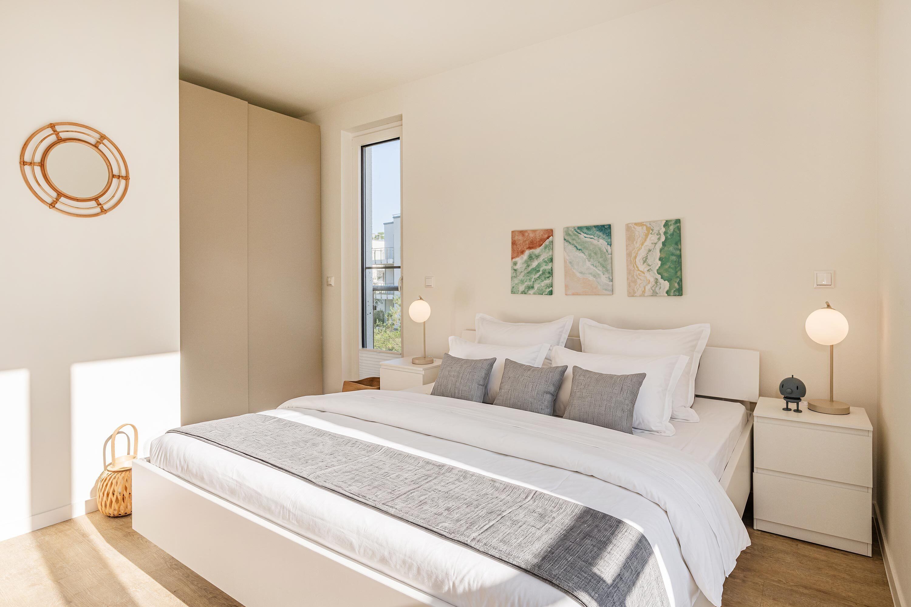 Ein modernes Schlafzimmer mit einem großen Bett, Nachttischen, einem Fenster und Kunstwerken an der Wand.
