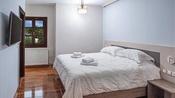 Un dormitorio con cama, mesita de noche, televisor montado en la pared, ventana con vistas y lámpara colgante.