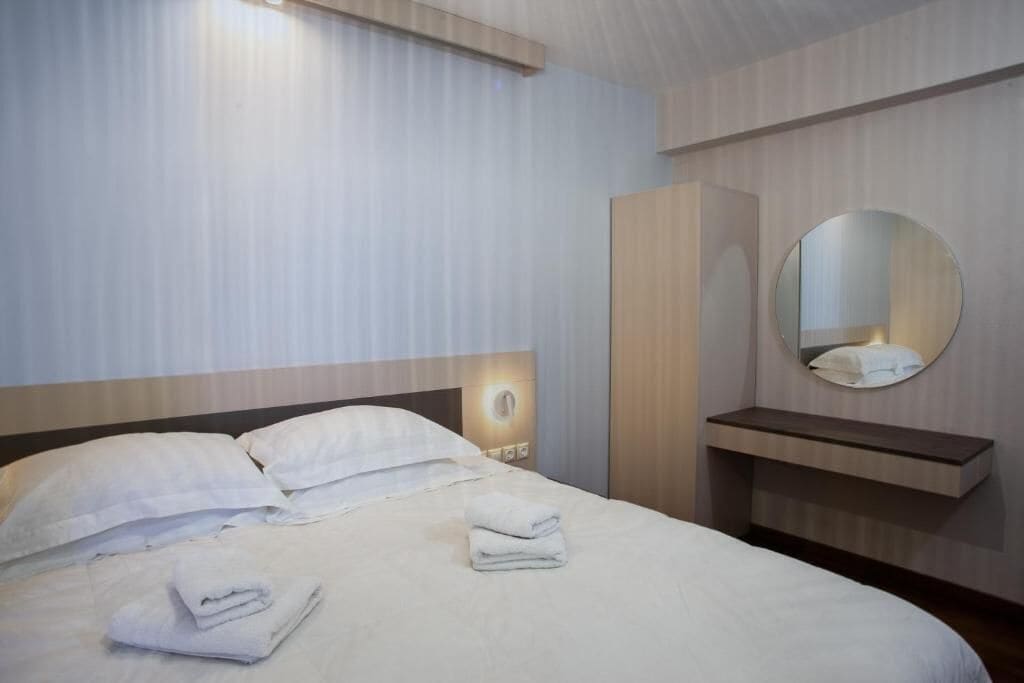 Een hotelkamer met een bed, nachtkastje, spiegel en garderobe.