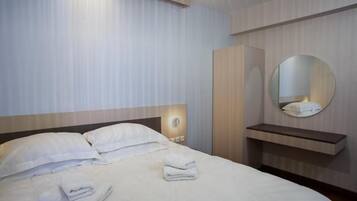 Een hotelkamer met een bed, nachtkastje, spiegel en garderobe.