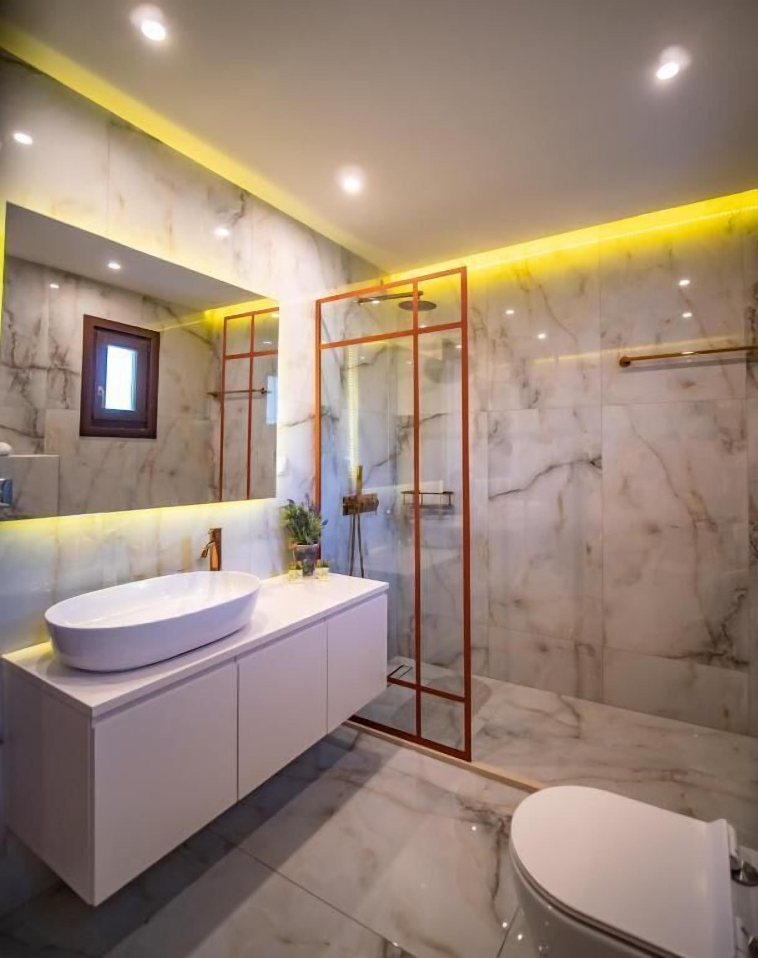 A modern bathroom with a marble vanity, a glass shower enclosure, and a toilet.