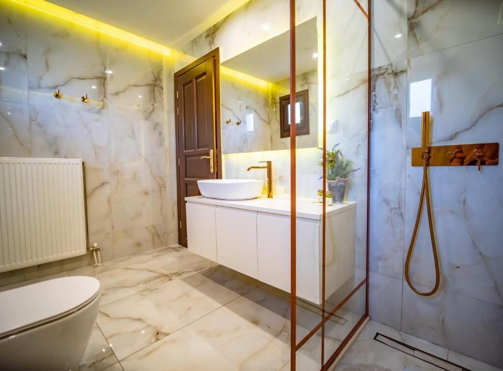 A bathroom with a marble floor, a white sink, a wooden cabinet, and a shower area.