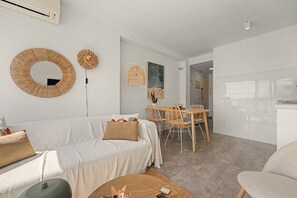 Ein modernes Wohnzimmer mit einer Couch, einem Esstisch und Stühlen. An der Wand befindet sich ein Spiegel und eine Hängelampe.