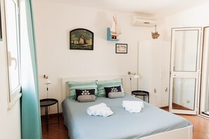A bedroom with a bed, pillows, a nightstand, a wall-mounted air conditioner, and a door. - Villa Tufara | Ocean View & Private Beach (San Vito)