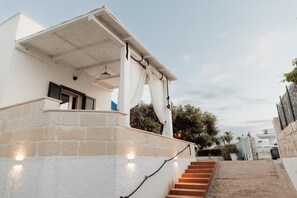 Un bâtiment à la façade en pierre, un escalier menant à une zone abritée et un ciel dégagé.