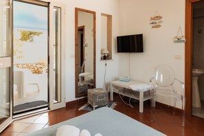 A room with a bed, a desk, a chair, a television, and a bathroom. - Villa Tufara | Ocean View & Private Beach (San Vito)