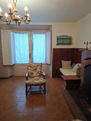 A room with a floral armchair, a bed with pillows, a wooden headboard, a chandelier, and a window with curtains. - A peaceful spot just a stone's throw from the Teso Forest.  
Dogs welcome. (Maresca)