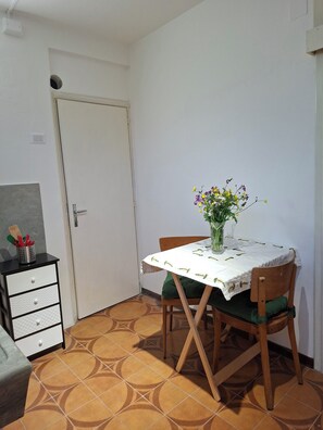 Ein Essbereich mit Tisch, Stühlen, einer Blumenvase, einem Schrank mit Besteck und einer Tür.