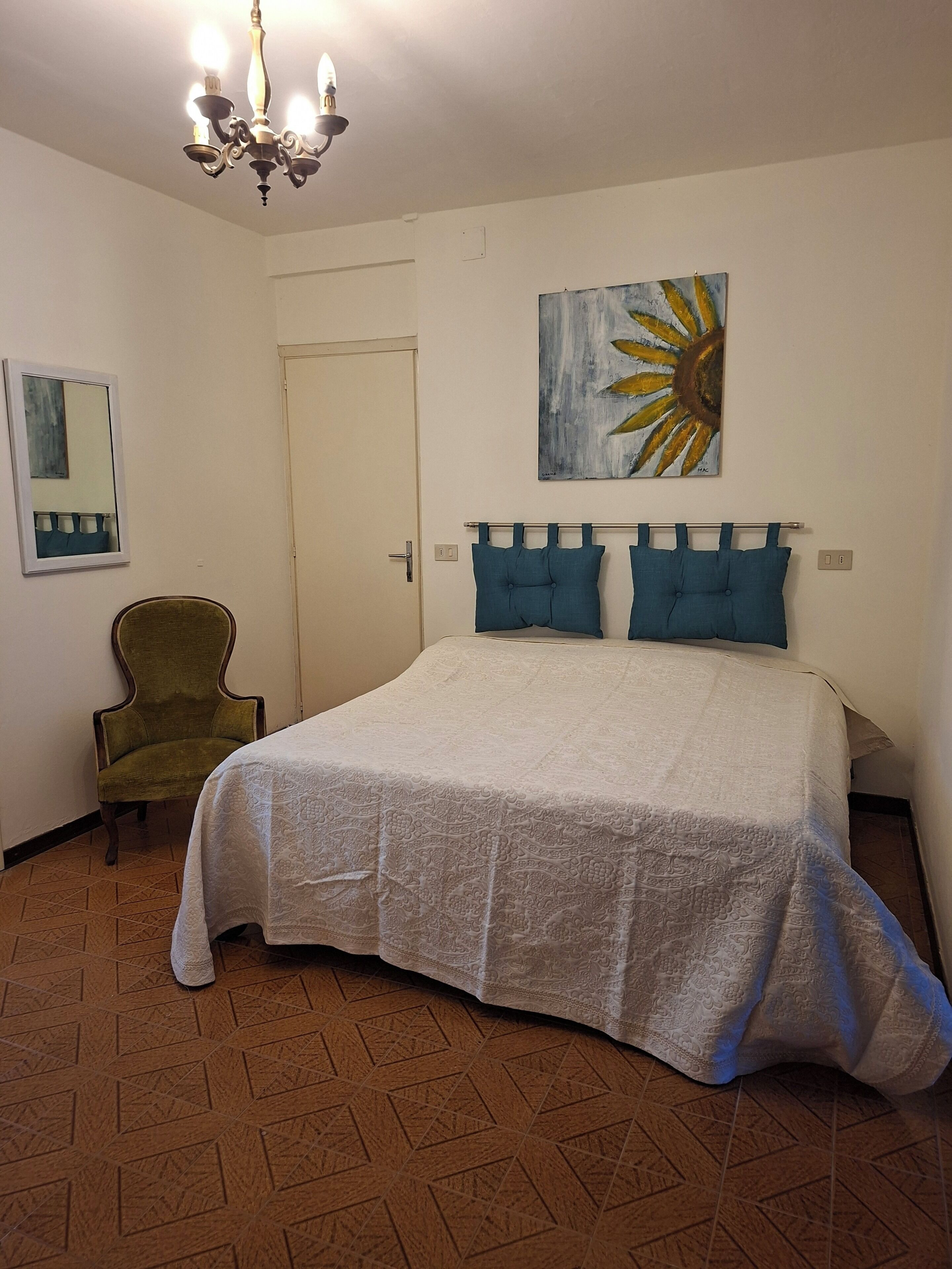 A bedroom with a bed, a chair, a painting, and a chandelier.