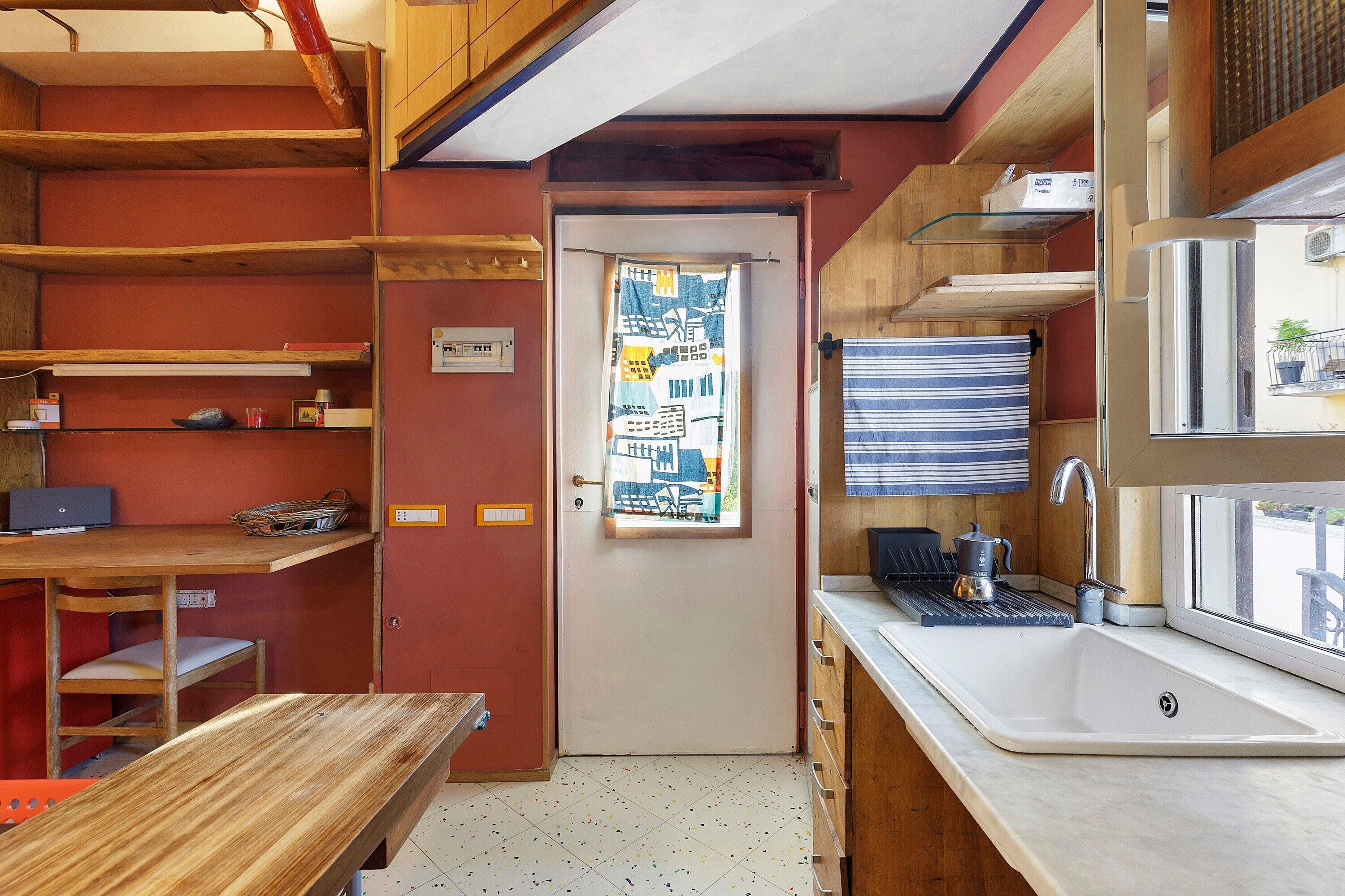 A compact kitchen with a sink, a window with a curtain, and a door with a light switch.
