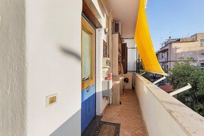 A narrow balcony with a blue door, a washing machine, and a yellow awning. - Romantic Studio 2 – Romantic Loft Near the City Center (Rome)
