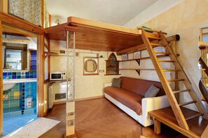 A compact living space with a wooden loft bed, a white sofa, and a ladder leading to a loft area. - Romantic Studio 2 – Romantic Loft Near the City Center (Rome)