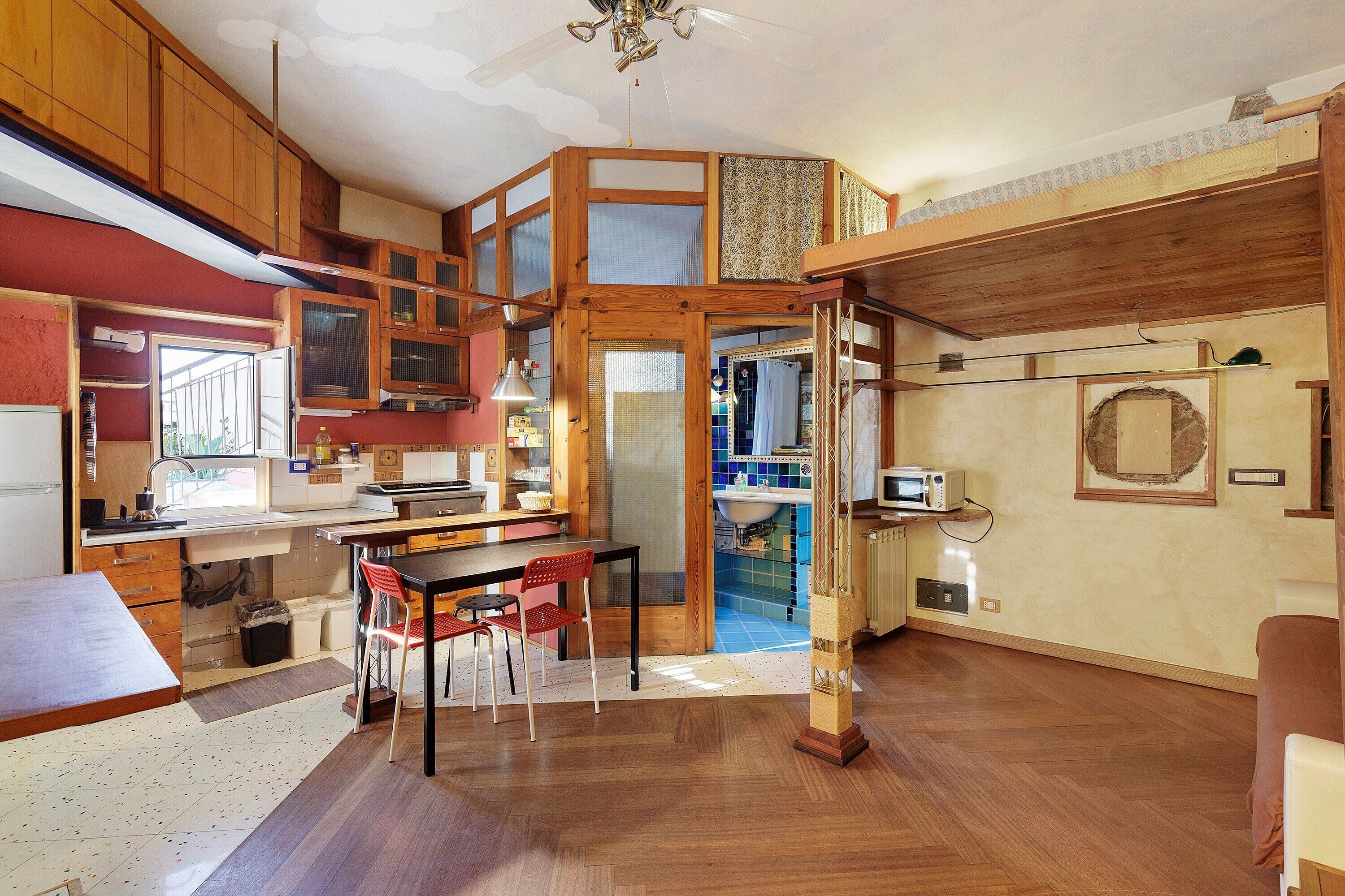 A compact kitchen with wooden cabinets, a dining area with a table and chairs, and a small bathroom with a sink and mirror.