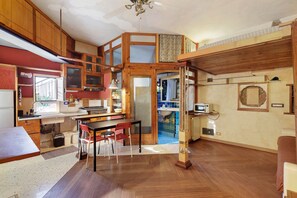 A compact kitchen with wooden cabinets, a dining area with a table and chairs, and a small bathroom with a sink and mirror. - Romantic Studio 2 – Romantic Loft Near the City Center (Rome)