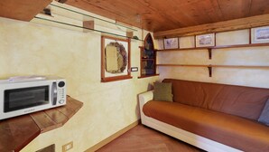 Ein gemütliches Zimmer mit Holzbalkendecke, einem weißen Sofa, einer Mikrowelle und gerahmten Bildern an der Wand.
