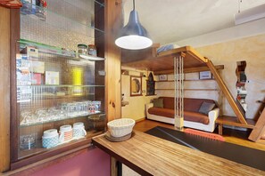 Um quarto acolhedor com escada de madeira, um sofá e uma vitrine de vidro com utensílios de cozinha.