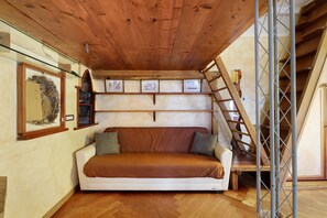 A room with a wooden ceiling, a white sofa with brown cushions, a ladder, and framed pictures on the wall. - Romantic Studio 2 – Romantic Loft Near the City Center (Rome)