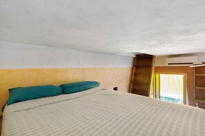 A bedroom with a bed, two pillows, a window with curtains, and an air conditioning unit. - Romantic Studio 2 – Romantic Loft Near the City Center (Rome)