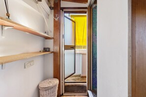 A narrow hallway with wooden shelves, a wicker basket, and a door leading to a room with a yellow curtain. - Cozy Studio Near Rome Center and Transport with View (Rome)
