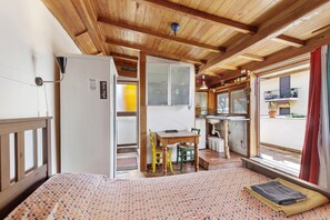 Una habitación con cama, una pequeña mesa con sillas, kitchenette y una ventana con cortinas.