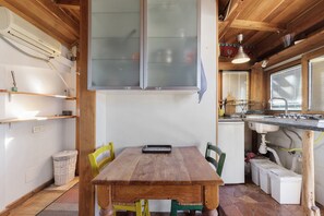 A wooden dining table with chairs, a kitchen area with a sink and stove, and a window with blinds. - Cozy Studio Near Rome Center and Transport with View (Rome)