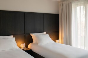 Ein Hotelzimmer mit einem großen Bett, zwei Nachttischen mit Lampen, einem dunklen Kopfteil und einem Fenster mit Vorhängen.