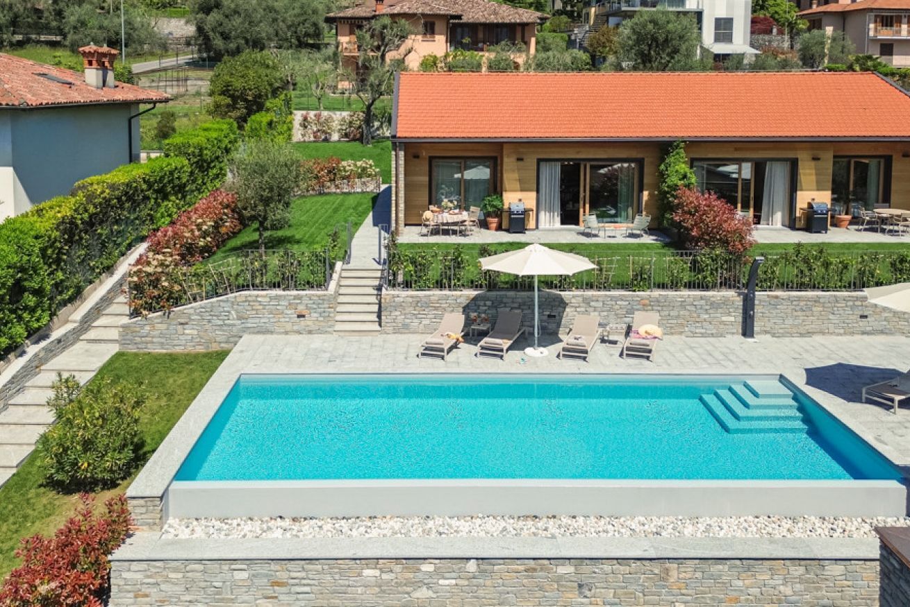 A rectangular swimming pool with a stone border, surrounded by a patio area with lounge chairs and a table.