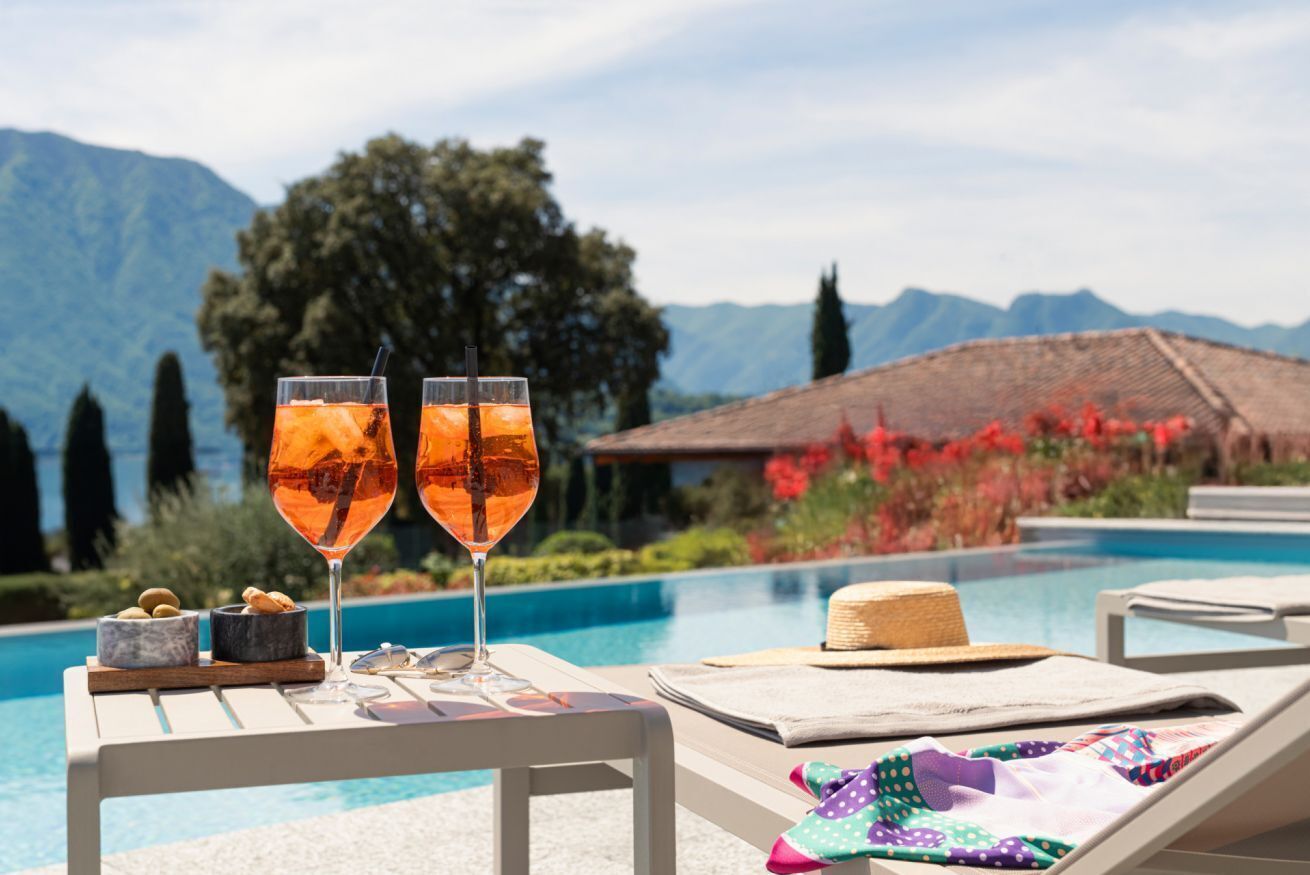 Une scène au bord de la piscine avec deux verres contenant une boisson, un chapeau et un coussin sur une chaise longue.