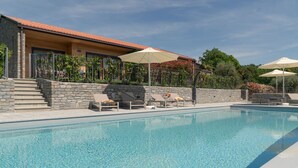 A swimming pool with lounge chairs and umbrellas, surrounded by a stone wall and a building with a tiled roof. - MC Lago - My Home in Como (Tremezzo)