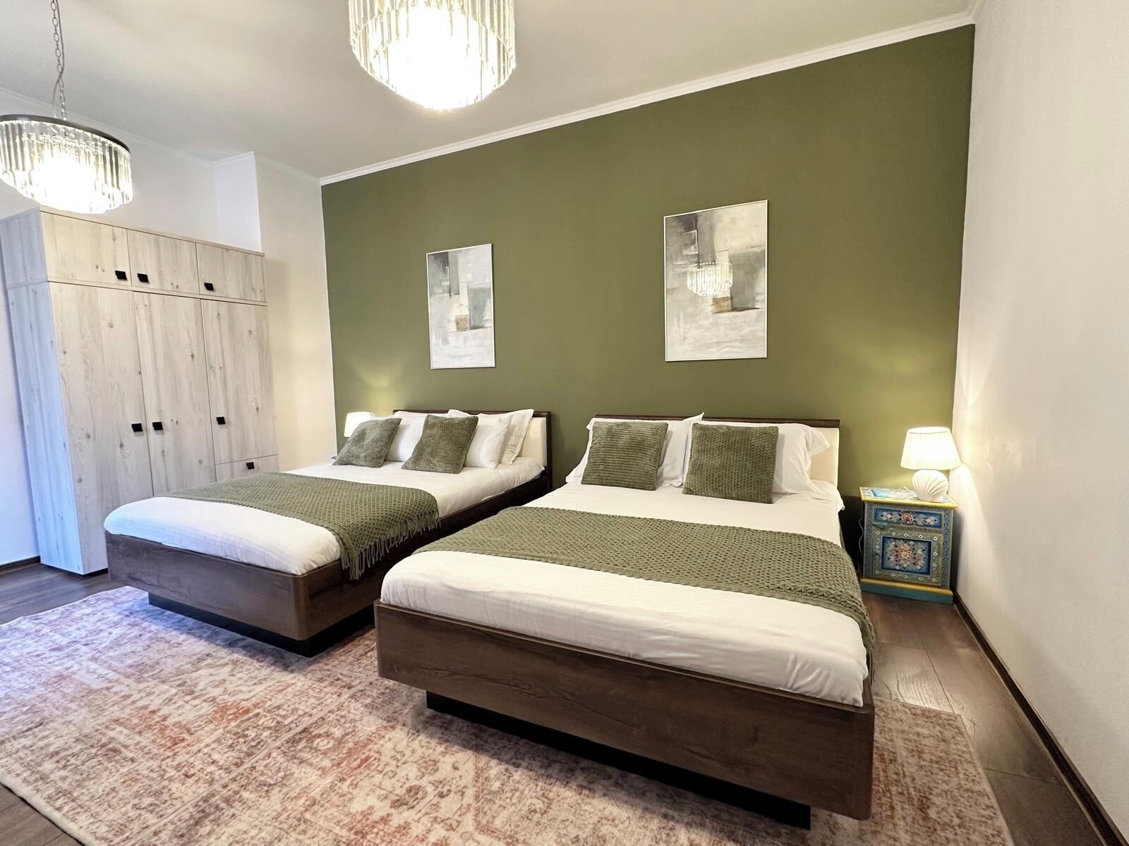 A bedroom with two beds, a wardrobe, and a nightstand with a lamp.