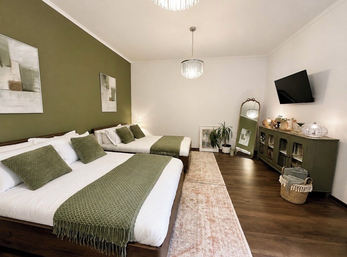 Un dormitorio con dos camas, una televisión, una araña y un aparador con objetos decorativos.