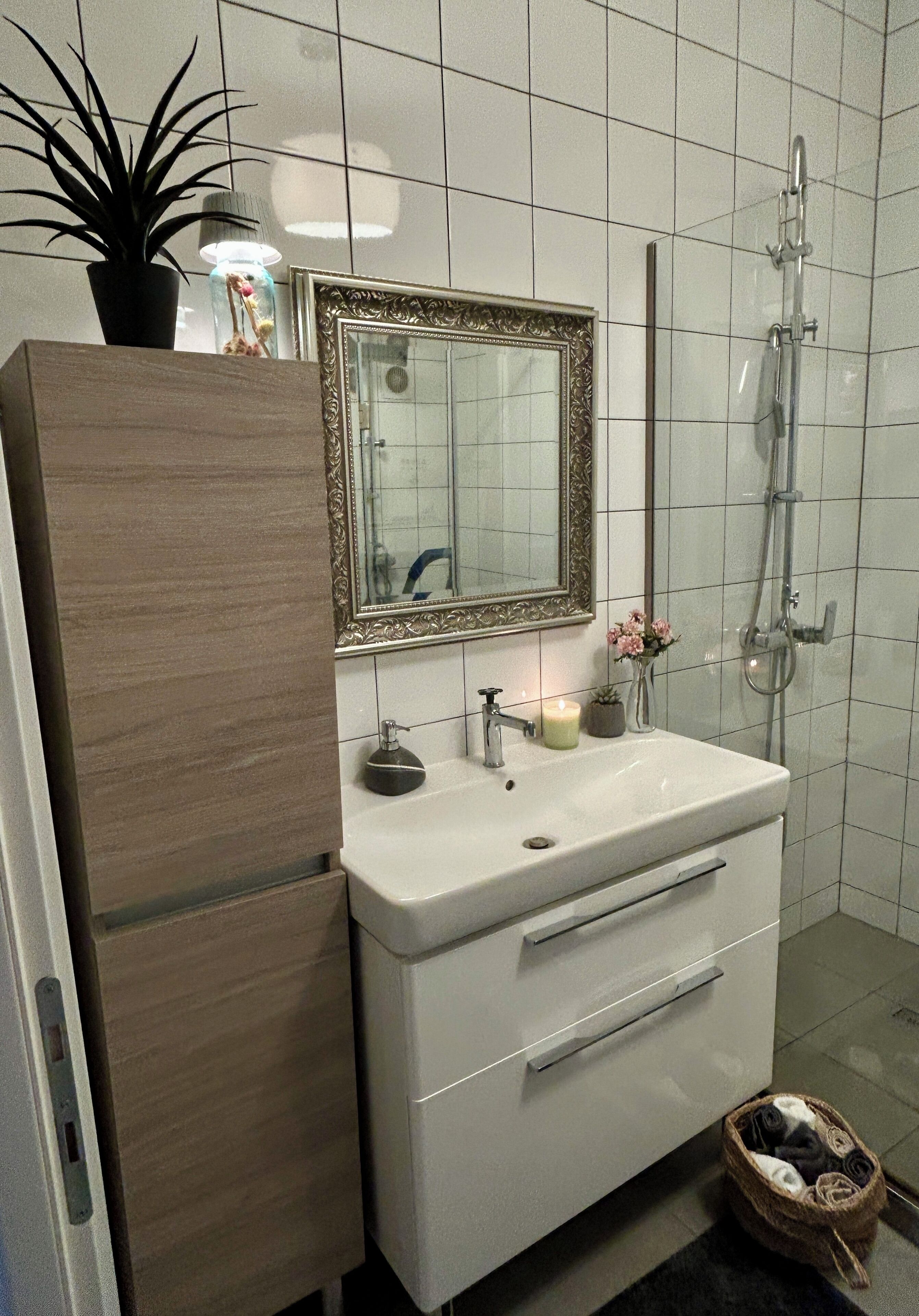 A bathroom with a white sink, a mirror with an ornate frame, a shower, and a wooden cabinet.