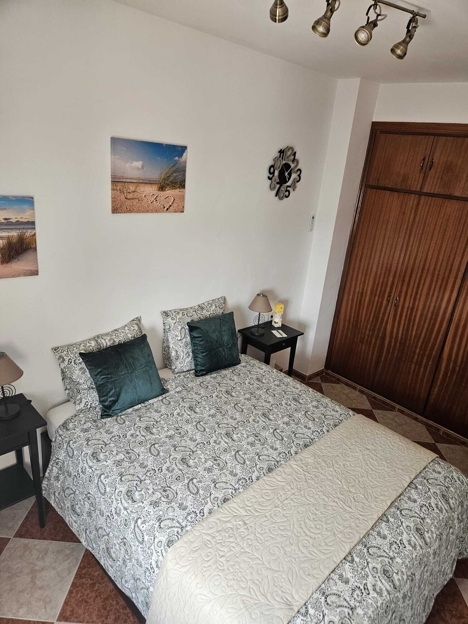 A bedroom with a bed, two bedside tables, a nightstand, a clock, and a wardrobe.