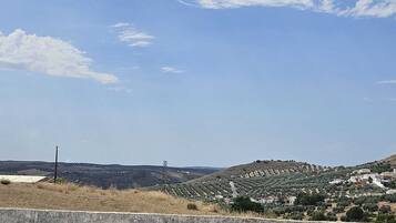 A rural landscape with a clear sky, a concrete barrier in the foreground, and a hilly area with buildings and vegetation.