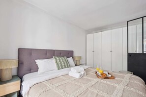 A neatly made bed with a grey headboard, white bedding, and a tray with breakfast items. - Charming 1BR near Louvre & Tuileries (Paris)