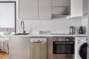 A modern kitchen with stainless steel appliances, including a dishwasher, oven, and washing machine. - Charming 1BR near Louvre & Tuileries (Paris)