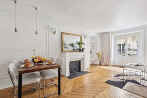 A dining area with a wooden table, chairs, and a fireplace. There is a window with a view of the outside. - Charming 1BR near Louvre & Tuileries (Paris)