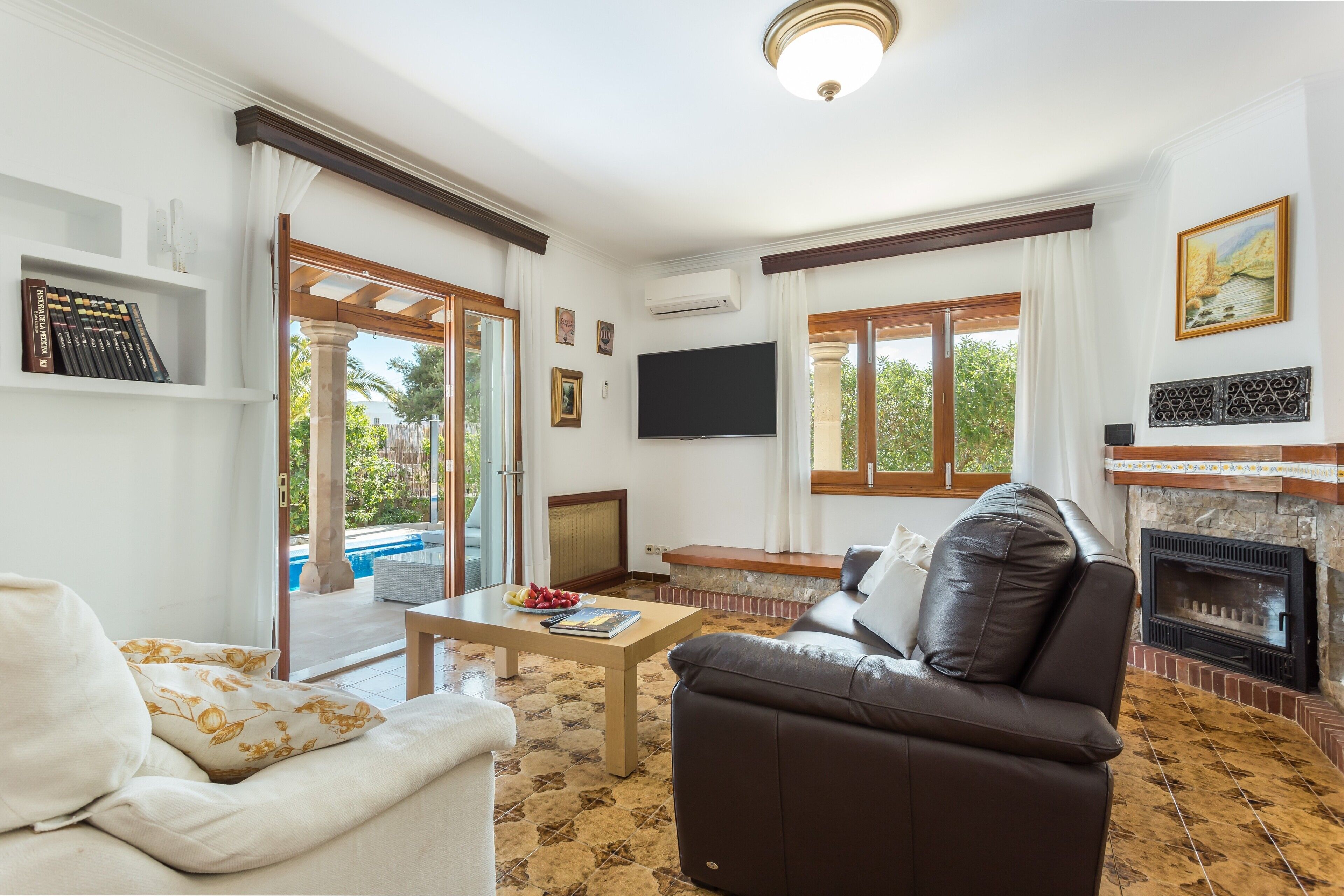 Ein Wohnzimmer mit Sofa, Couchtisch, Kamin, Fernseher und Blick ins Freie.