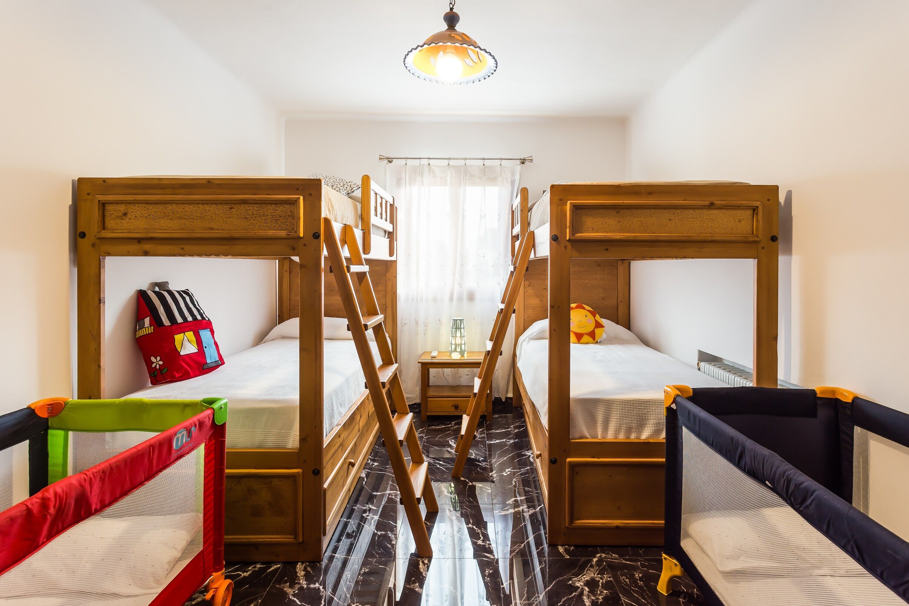 Ein Zimmer mit zwei Etagenbetten, einem kleinen Tisch, einer Hockerleiter und einem Reisebett.