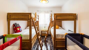 Ein Zimmer mit zwei Etagenbetten, einem kleinen Tisch, einer Hockerleiter und einem Reisebett.