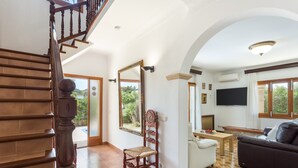 A spacious living area with a wooden staircase, a large mirror, a sofa, a television, and a dining table. - Villa 'Russadir' with Private Pool, Wi-Fi and Air Conditioning (Santanyí)