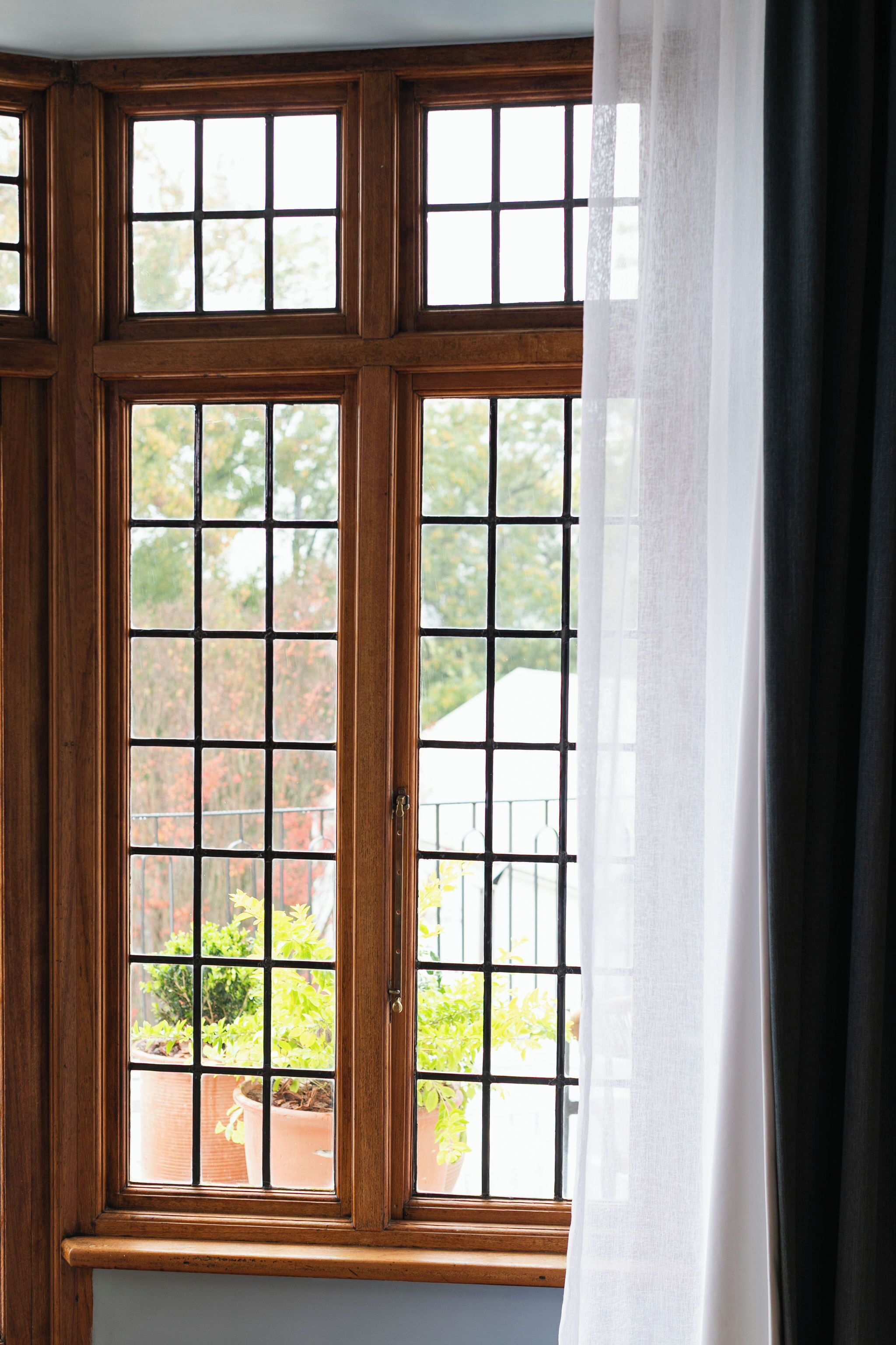 Una ventana con un diseño de cuadrícula, marco de madera y una cortina entreabierta.